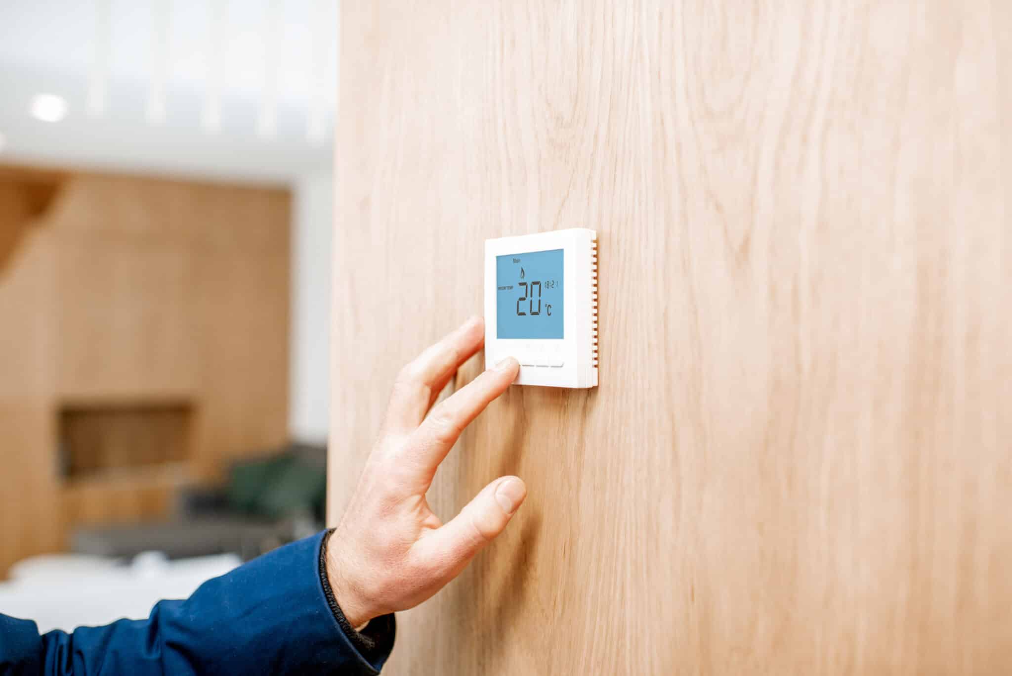Nicolas de New Clim, expert en climatisation, règle un thermostat à 20°c.